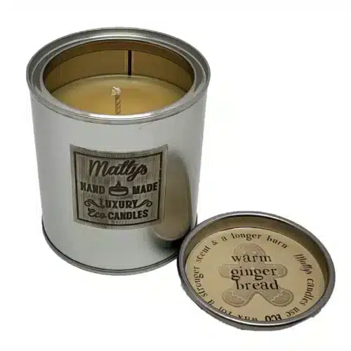 A silver tin "Gingerbread Scented Candle" by Matty's Handmade Luxury Eco Candles sits with the lid off, revealing the wick. The lid notes “warm gingerbread,” plus a stronger scent and longer burn time.