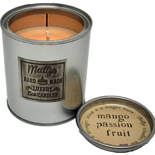 A silver tin candle labeled "Mango and Passion Fruit Scented Candle" burns with a lit wick, while the lid nearby displays details of its tropical fragrance and burn time, creating an inviting and exotic ambiance.
