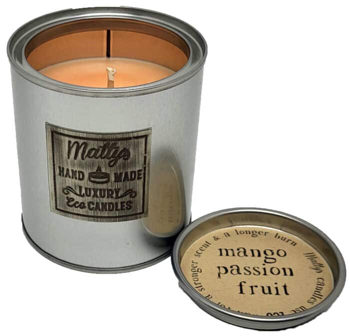 A silver tin candle labeled "Mango and Passion Fruit Scented Candle" burns with a lit wick, while the lid nearby displays details of its tropical fragrance and burn time, creating an inviting and exotic ambiance.