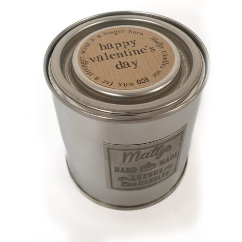 A silver metal can with a label that reads "Matty's Hand Made Luxury Eco Candles." The lid has a circular label with the message "Happy Valentine's Day" and mentions the use of eco wax for a "longer burn" and "a lovelier scent.