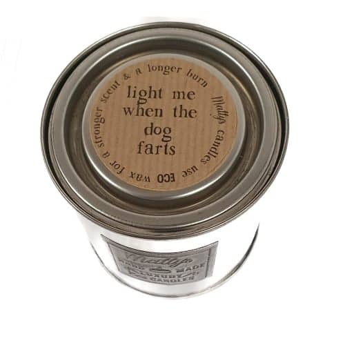 A silver tin candle with a beige label that reads "light me when the dog farts" in bold black text. Branded as "Light me when the dog farts Labels x 24," it boasts eco wax for a longer burn and a stronger scent, making it the perfect remedy when your furry friend clears the room.