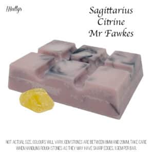 A bar of pink soap embedded with black swirls, shown alongside a yellow citrine gemstone. The text reads, "Mr Fawkes Sagittarius Citrine Gem Stone Snap Bar." A disclaimer at the bottom mentions that colors will vary, gemstone sizes are between 8mm and 20mm, and there is one citrine gem stone per snap bar.