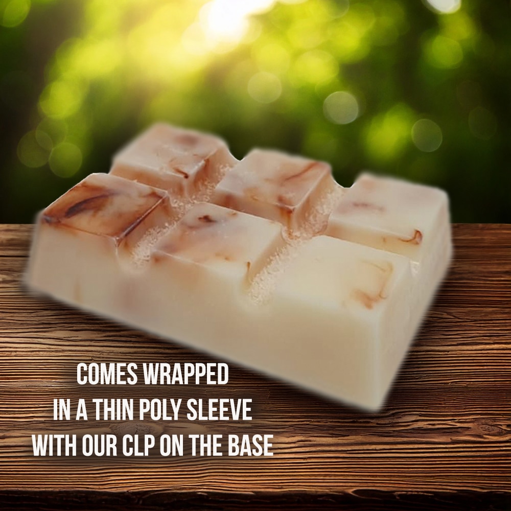 A handcrafted soap block with a marbled texture rests on a wooden surface. The background is blurred greenery. Text on the image reads: "Comes wrapped in a thin poly sleeve with our CLP on the base.