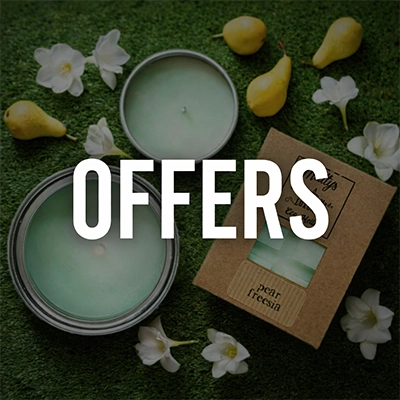 A green candle in a tin, its lid off, sits on grass with white flowers and small pears nearby. A "pear freesia" box is beside it. “OFFERS” is overlaid in bold white letters—perfect for lovers of candles and wax melts.